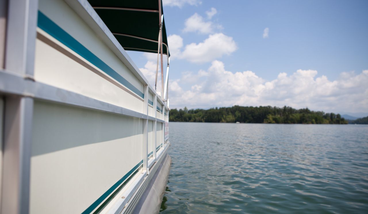Close-up of the side of a Granbury pontoon rental on the Lake Granbury water and a sunny day in the background